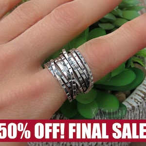May include: A silver ring with a textured, multi-band design. The ring is worn on a finger, showcasing its intricate, layered appearance. The ring's surface has a hammered texture, adding to its unique aesthetic. The ring is a piece of jewelry.