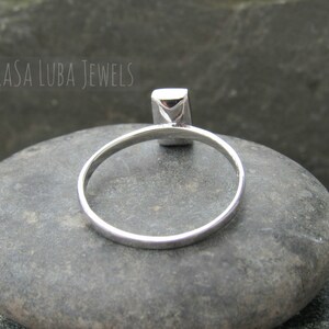 May include: A silver ring with a square-shaped gemstone. The ring is sitting on a gray rock.