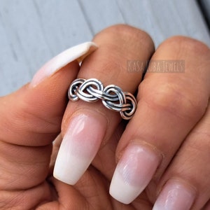 May include: A silver ring with a braided design. The ring is worn on a finger with white nail polish.