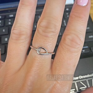 May include: A silver ring with a heart-shaped design. The ring is worn on a person's finger.
