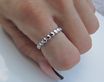 May include: A silver ring with a band of small heart-shaped beads. The ring is worn on a finger.