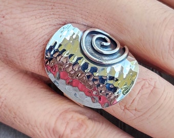 May include: A silver ring with a hammered finish and a spiral design. The ring is wide and has a rounded shape.