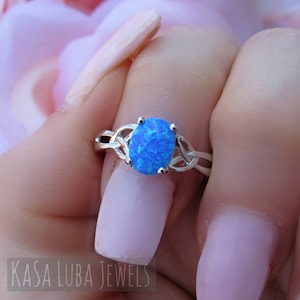 May include: A silver ring with a blue opal gemstone set in a Celtic knot design.