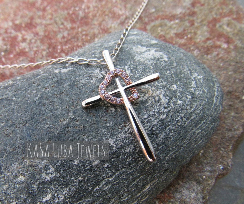 Puede incluir: Un collar de plata y oro rosa con un colgante de cruz en forma de coraz&oacute;n. La cruz est&aacute; adornada con piedras de circonita c&uacute;bica transparentes.