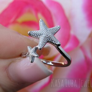 May include: Silver ring with two textured starfish designs. The larger starfish is on top of the smaller starfish. The ring is open and adjustable.