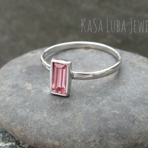 May include: A silver ring with a pink rectangular gemstone. The ring is on a gray stone surface. KASA LUBA JEWELS is written in the background.