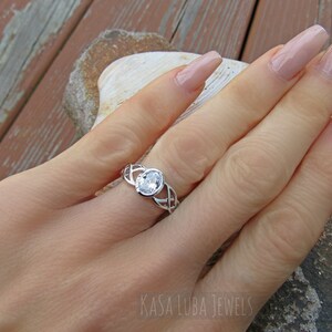 K&ouml;nnte beinhalten: Ein silberner Ring mit einem ovalen, klaren Edelstein. Der Ring hat ein keltisches Knotenmuster auf dem Band. Der Text "KASA LUBA JEWELS" ist unten rechts im Bild zu sehen.