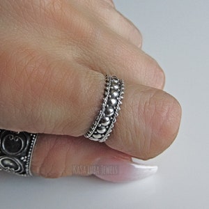 May include: A silver ring with a beaded design. The ring is worn on a finger.