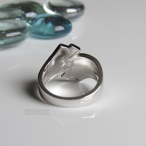 Op de afbeelding: Een zilveren ring met een bliksemontwerp. De ring wordt van achteren getoond, met de band zichtbaar.