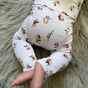 Könnte beinhalten: Weiße Baby-Leggings mit einem braunen und weißen Fruchtmuster. Die Leggings sind an den Knöcheln hochgekrempelt.