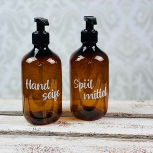 May include: Two amber glass bottles with black pump tops and white labels. The bottle on the left says "Hand Seife" and the bottle on the right says "Sp&uuml;lmittel".