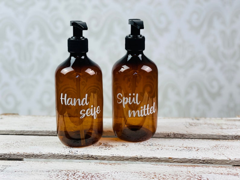 May include: Two amber glass bottles with black pump tops and white labels. The bottle on the left says "Hand Seife" and the bottle on the right says "Sp&uuml;lmittel".