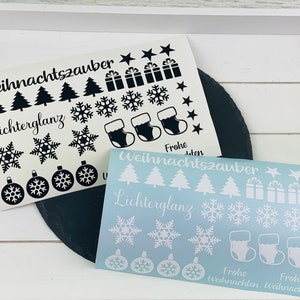 Könnte beinhalten: Zwei Bögen mit weihnachtlichen Stickern. Ein Bogen ist weiß mit schwarzen Designs und der andere ist hellblau mit weißen Designs. Beide Bögen zeigen Weihnachtsbäume, Schneeflocken, Ornamente, Strümpfe und Geschenkboxen. Der Text "Weihnachtszauber" und "Lichterglanz" befindet sich auf beiden Bögen.