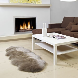 May include: A white coffee table with a lower shelf sits in a living room with a brown sectional sofa, a fireplace, and a beige sheepskin rug.