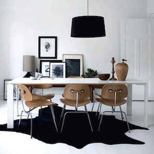 May include: A white dining table with four wooden chairs and a black cowhide rug. A black pendant light hangs above the table. There are framed black and white photos on the wall behind the table.