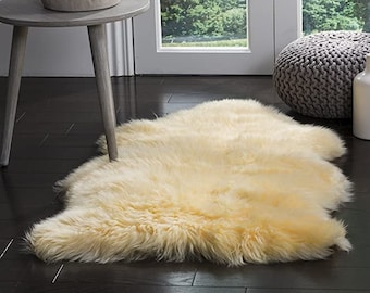 May include: A fluffy, cream-colored sheepskin rug with a long pile. The rug is laid out on a hardwood floor in a living room setting.