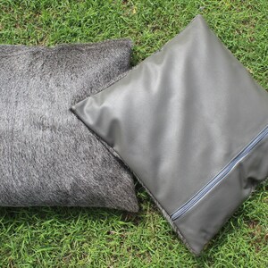 May include: Two decorative throw pillows, one gray and fuzzy, the other gray and smooth with a zipper detail.