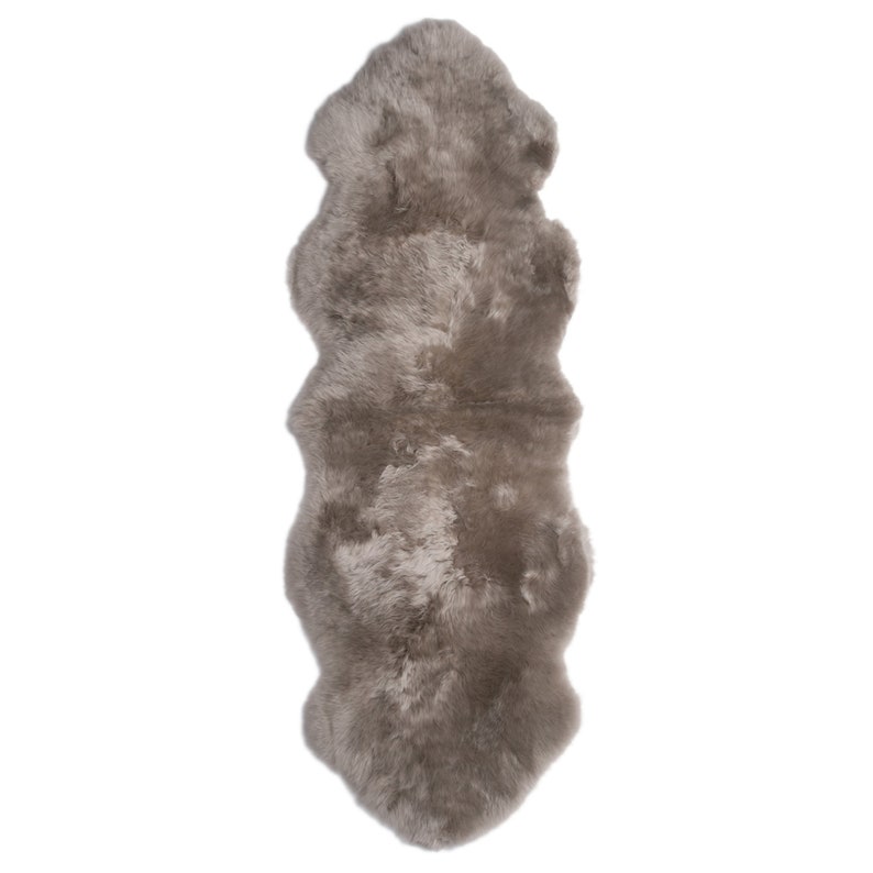 May include: A long, rectangular sheepskin rug in a light gray color. The rug has a soft, fluffy texture and is perfect for adding warmth and comfort to any room.