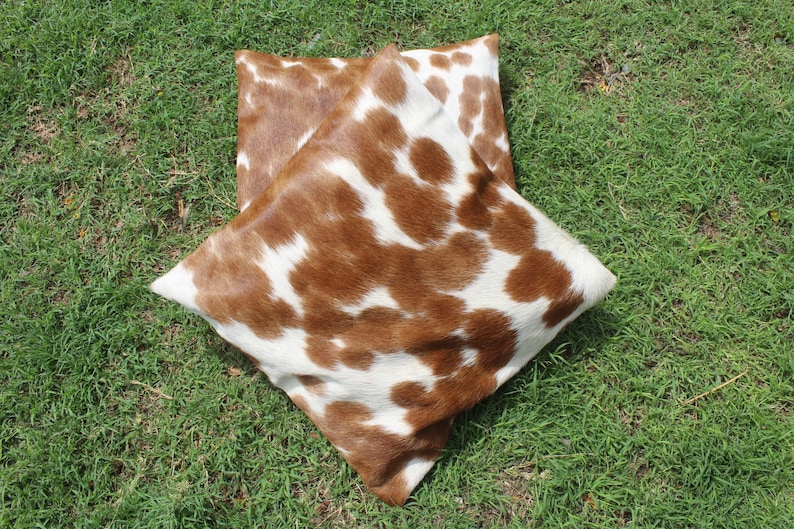 May include: Two brown and white cowhide throw pillows with a soft, fuzzy texture.