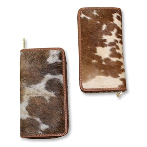 Puede incluir: Dos carteras de cuero marr&oacute;n con un patr&oacute;n de piel de vaca blanca y marr&oacute;n. Las carteras tienen cierre de cremallera.