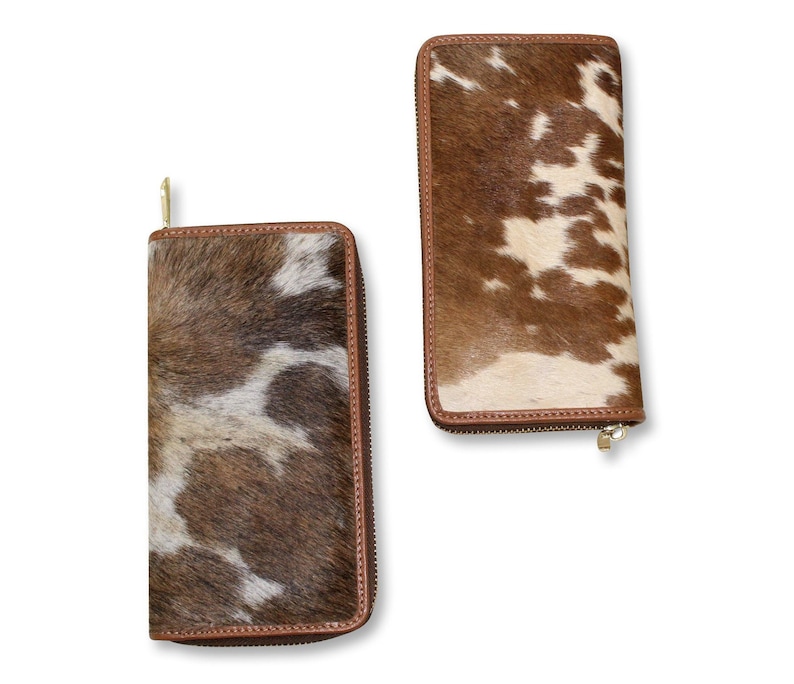 Puede incluir: Dos carteras de cuero marr&oacute;n con un patr&oacute;n de piel de vaca blanca y marr&oacute;n. Las carteras tienen cierre de cremallera.