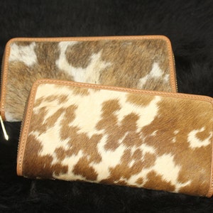 Puede incluir: Dos carteras con cremallera de cuero de vaca marr&oacute;n y blanco. Las carteras tienen un ribete de cuero marr&oacute;n y una cremallera dorada.