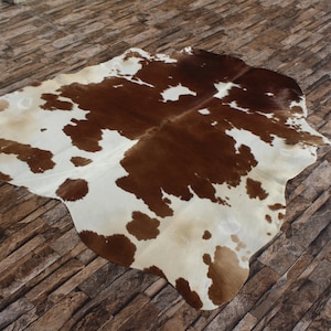 May include: A brown and white cowhide rug with a natural, irregular shape. The rug has a patchwork pattern of brown and white patches.
