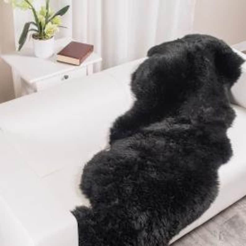 May include: Black sheepskin rug with a wavy shape, perfect for adding a touch of warmth and texture to any room.