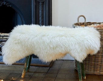 May include: A white sheepskin rug is draped over a wooden stool with green painted legs. The stool is in front of a black fireplace and a wicker basket. A string of fairy lights is on the wooden floor.