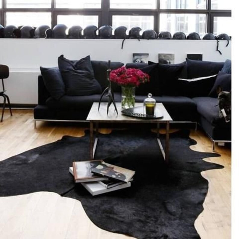 May include: A black leather cowhide rug with a black leather sofa and a coffee table with a vase of red roses in the background.