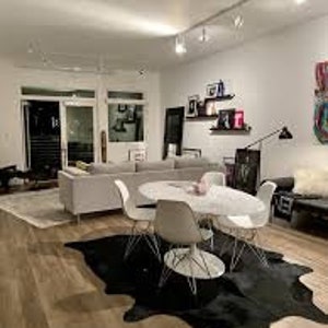 May include: A white dining table with four white chairs and a black cowhide rug. The table is set with a white vase and flowers. The room has a modern design with white walls and a wood floor.