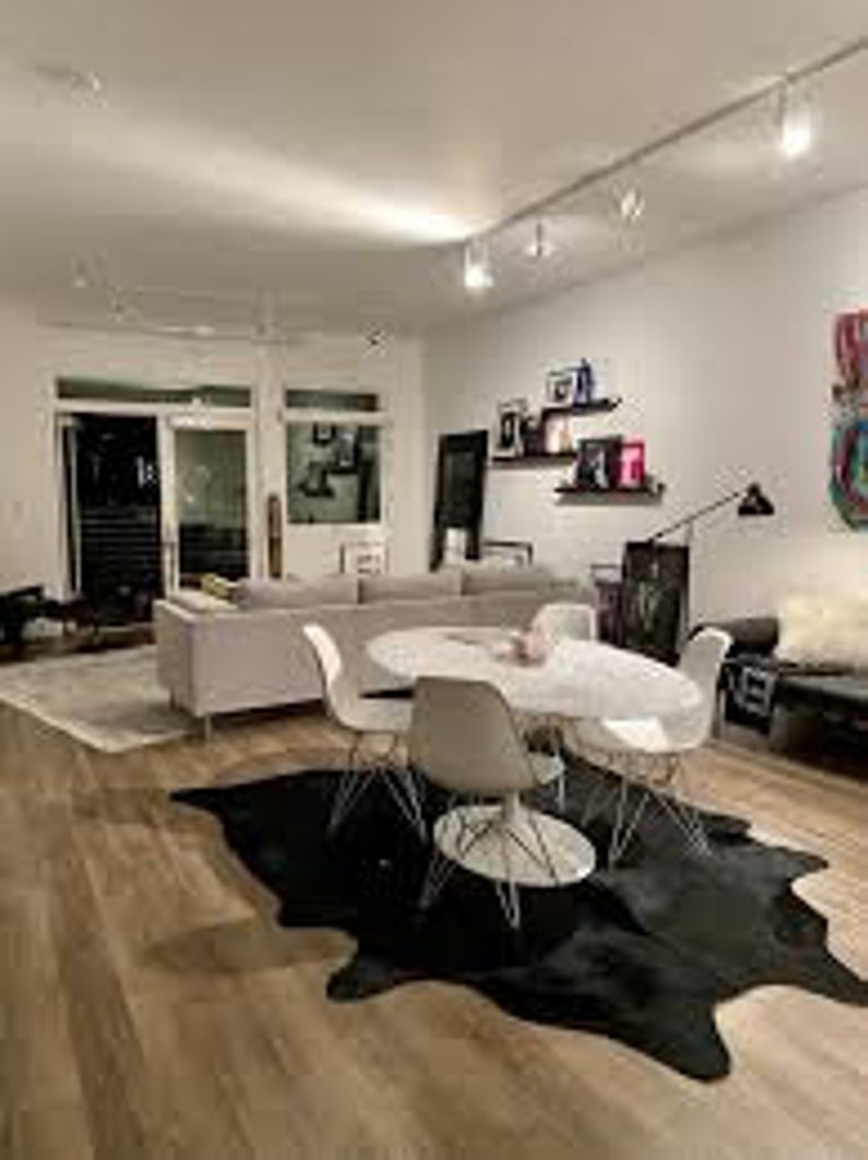 May include: A white dining table with four white chairs and a black cowhide rug. The table is set with a white vase and flowers. The room has a modern design with white walls and a wood floor.