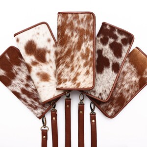 May include: Five brown and white cowhide wallets with brown leather straps. The wallets are arranged in a fan shape with the straps hanging down.