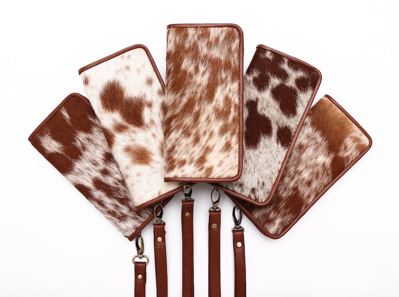 May include: Five brown and white cowhide wallets with brown leather straps. The wallets are arranged in a fan shape with the straps hanging down.