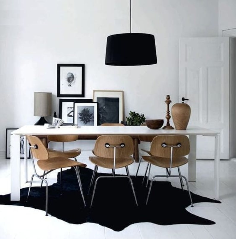 May include: A white dining table with four wooden chairs and a black cowhide rug. A black pendant light hangs above the table. There are framed black and white photos on the wall behind the table.