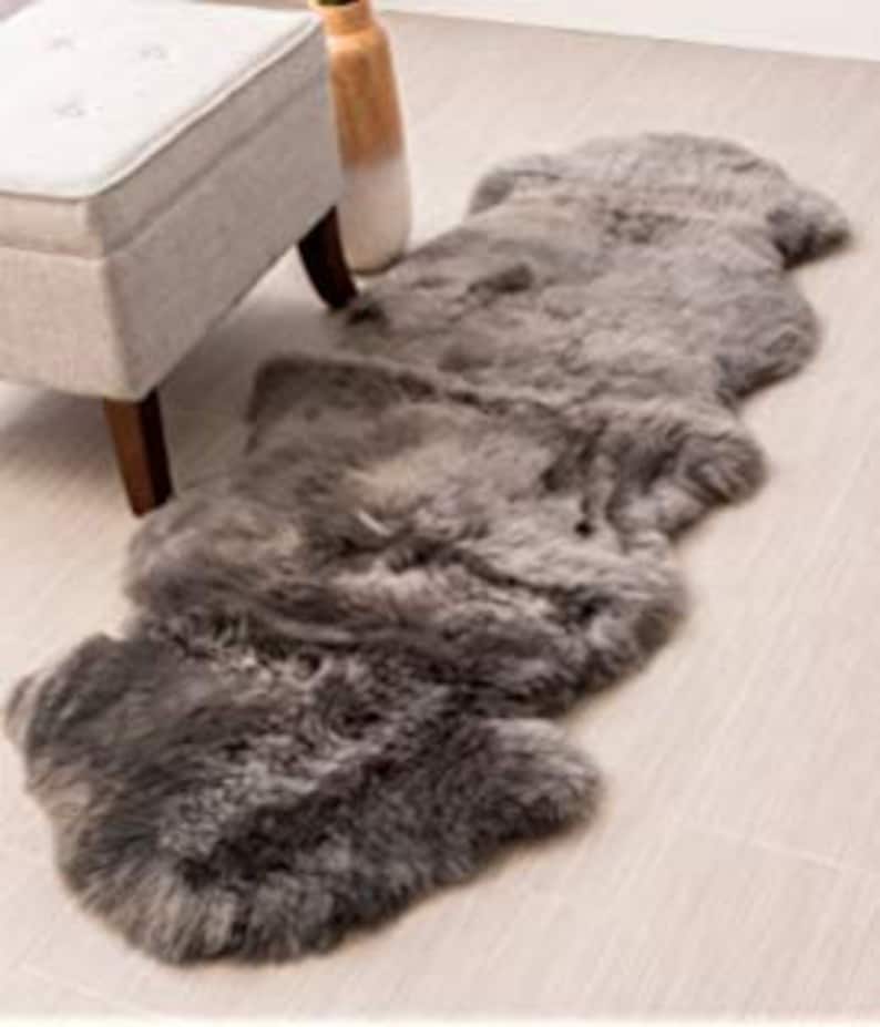 May include: A long, gray sheepskin rug with a soft, fluffy texture. The rug is made of natural sheepskin and is perfect for adding warmth and comfort to any room.