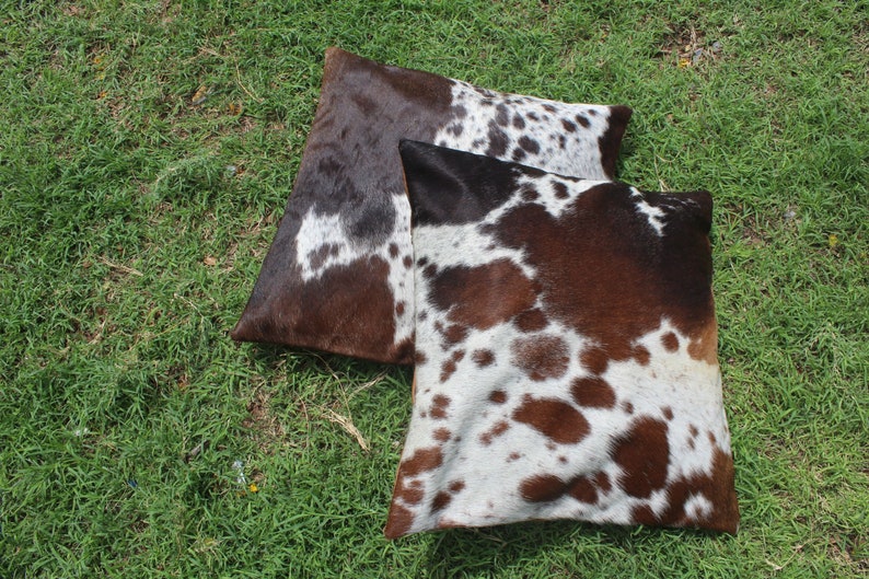 May include: Two brown and white cowhide throw pillows with a spotted pattern.