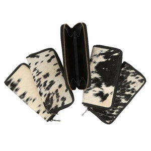 May include: Five black and white cowhide wallets with black zips. The wallets are laid out on a white background.