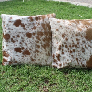May include: Two brown and white cowhide throw pillows with a spotted pattern.