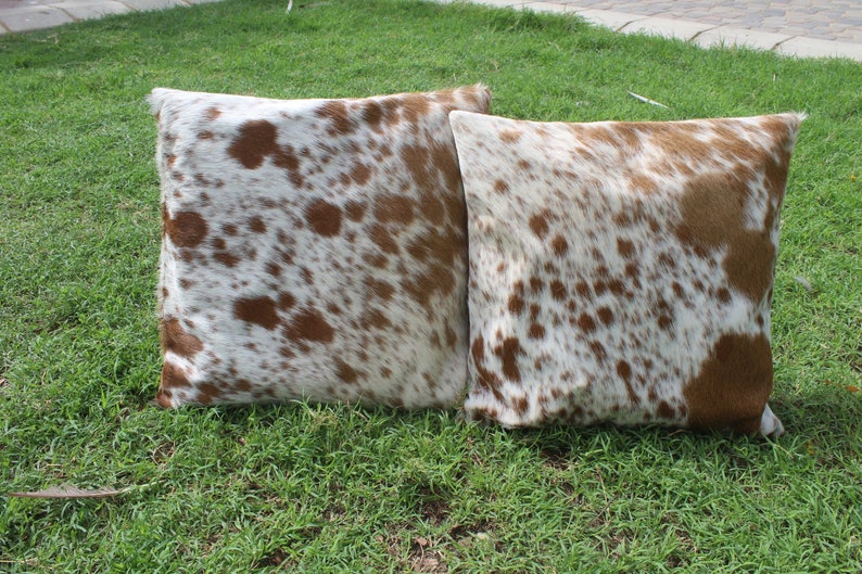 May include: Two brown and white cowhide throw pillows with a spotted pattern.