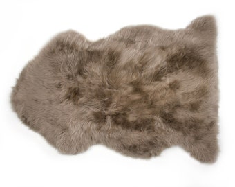 May include: A soft, brown sheepskin rug with a natural, fluffy texture. The rug is shaped like a hide and has a natural, irregular shape.