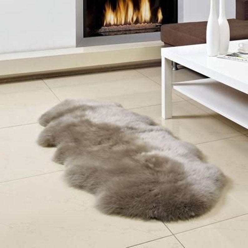 May include: A light brown sheepskin rug with a long, rectangular shape. The rug is soft and fluffy, and it has a natural, rustic look.