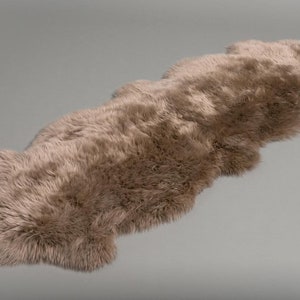 May include: A long, light brown sheepskin rug with a fluffy texture. The rug is laid out flat on a gray background.