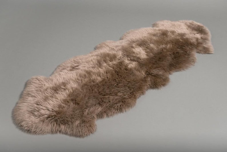 May include: A long, light brown sheepskin rug with a fluffy texture. The rug is laid out flat on a gray background.