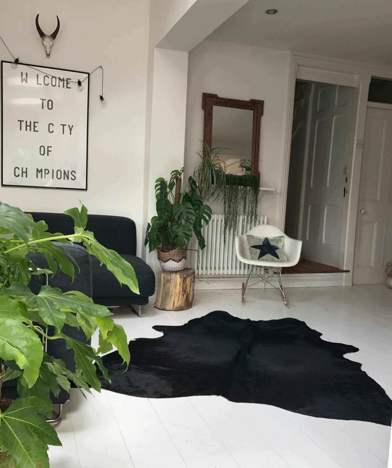 May include: A black cowhide rug with a white background. The rug is in a living room with a black sofa, a white chair, and a plant in a brown pot. There is a sign on the wall that says "Welcome to the City of Champions".