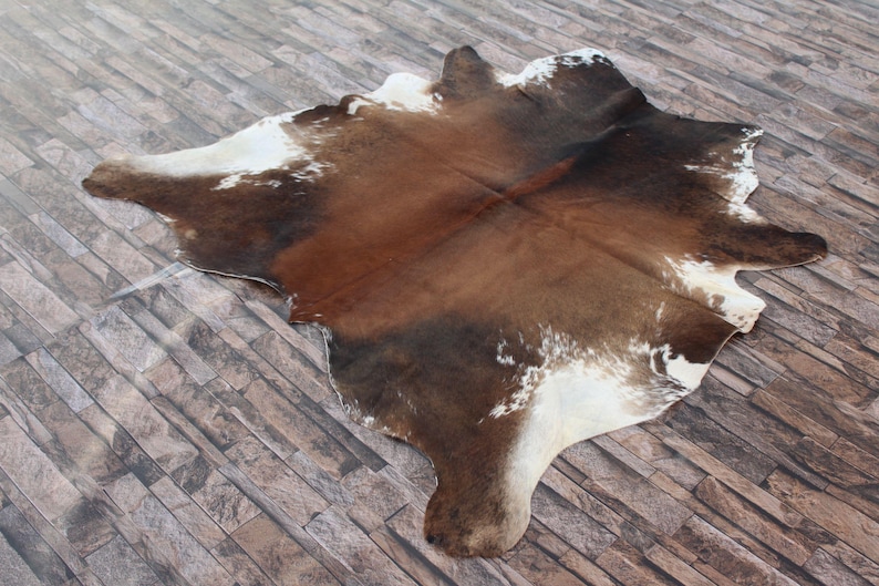 May include: A brown and white cowhide rug with a natural, rustic look. The hide has a patchwork pattern of brown and white patches.