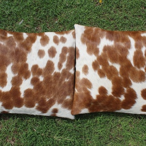 May include: Two brown and white cowhide throw pillows with a soft, fuzzy texture.