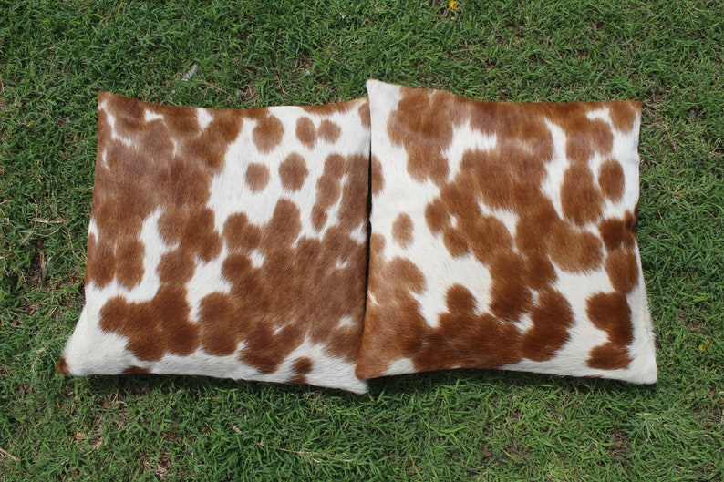 May include: Two brown and white cowhide throw pillows with a soft, fuzzy texture.