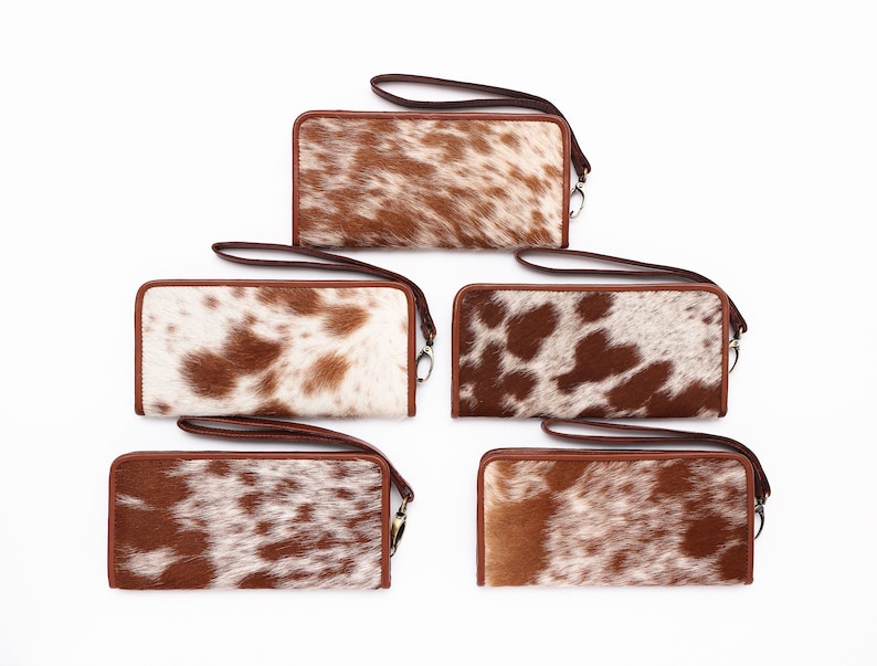 May include: Five brown and white cowhide wallets with brown leather trim and a wrist strap.