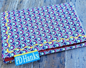 May include: A small, blue fabric wallet with a yellow stitched border and a repeating pattern of blue and purple hearts. The wallet has a blue label with the text "PD Hanks" on it.